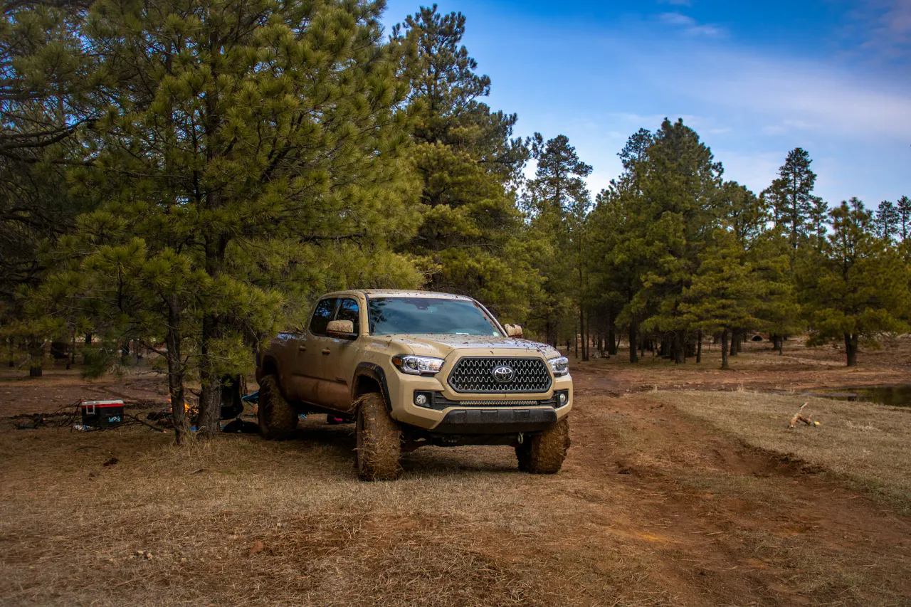 Muddy tires on a Toyota Pick up truck parked on a dirt road by pine trees.