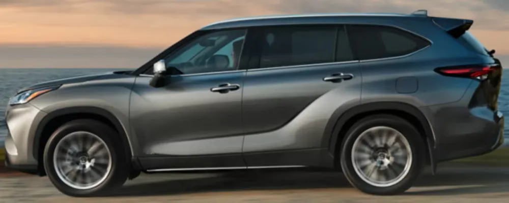 A silver Highlander Hybrid drives along the coast at sunrise