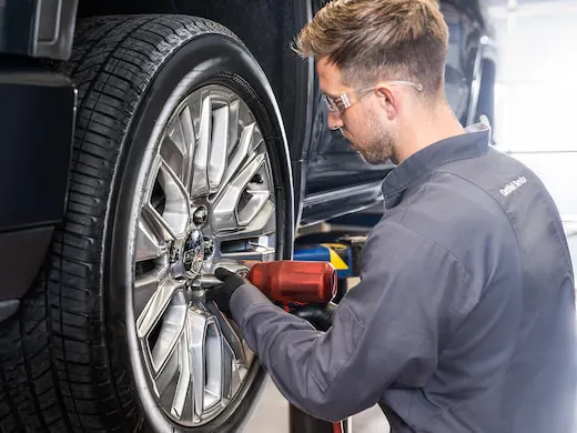 Service technician uses impact wrench to install wheel to car