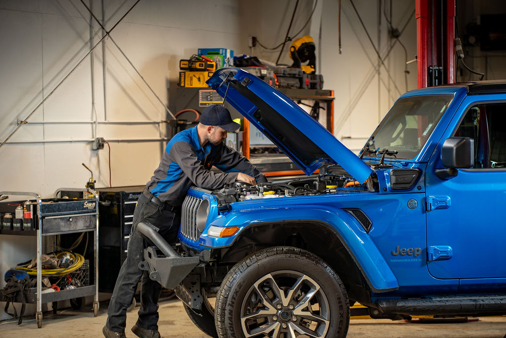 Technician working under the hood of a blue Jeep Wrangler in the Juneau Auto Mall service shop