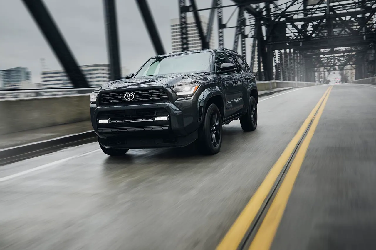 2025 Toyota 4Runner in dark gray driving across a wet steel bridge in the rain
