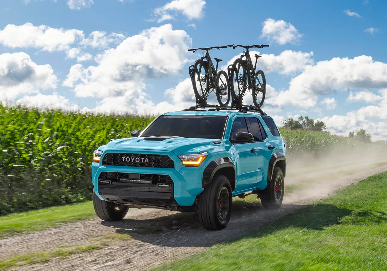 2026 Toyota 4Runner TRD Pro in light blue loaded with mountain bikes on roof rack driving a rural dirt road