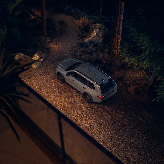 White Toyota Grand Highlander driving down a tree-lined road at dusk