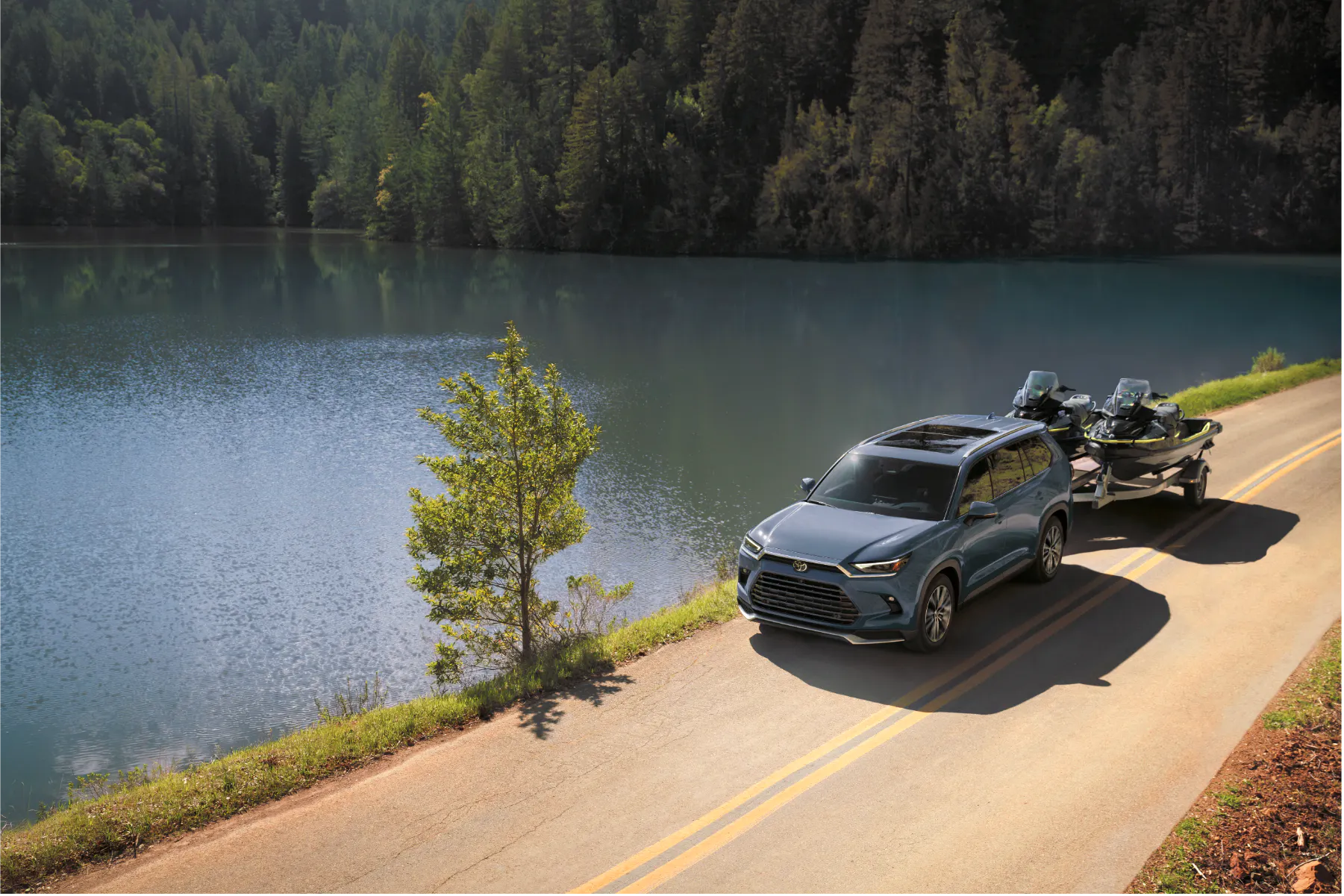 Blue Toyota Grand Highlander towing two jet skis on a trailer near a lake