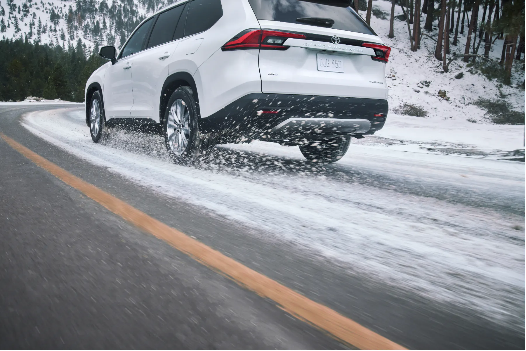 White Toyota Grand Highlander driving through snow with powder kicking up behind the tires