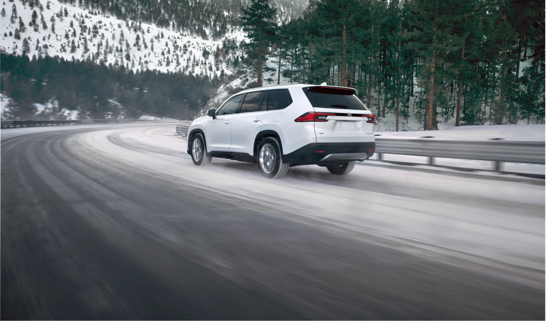 Rear view of a white Toyota Grand Highlander on a snowy mountain road
