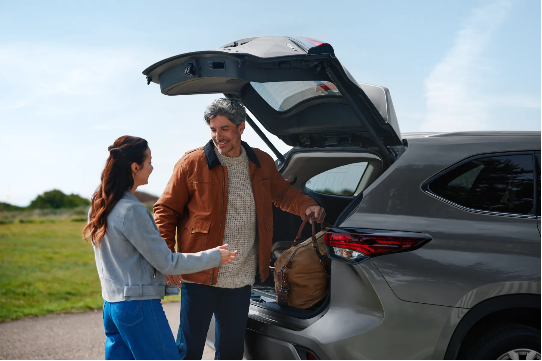 Smiling couple loading a duffel bag into the rear of a silver Toyota Highlander