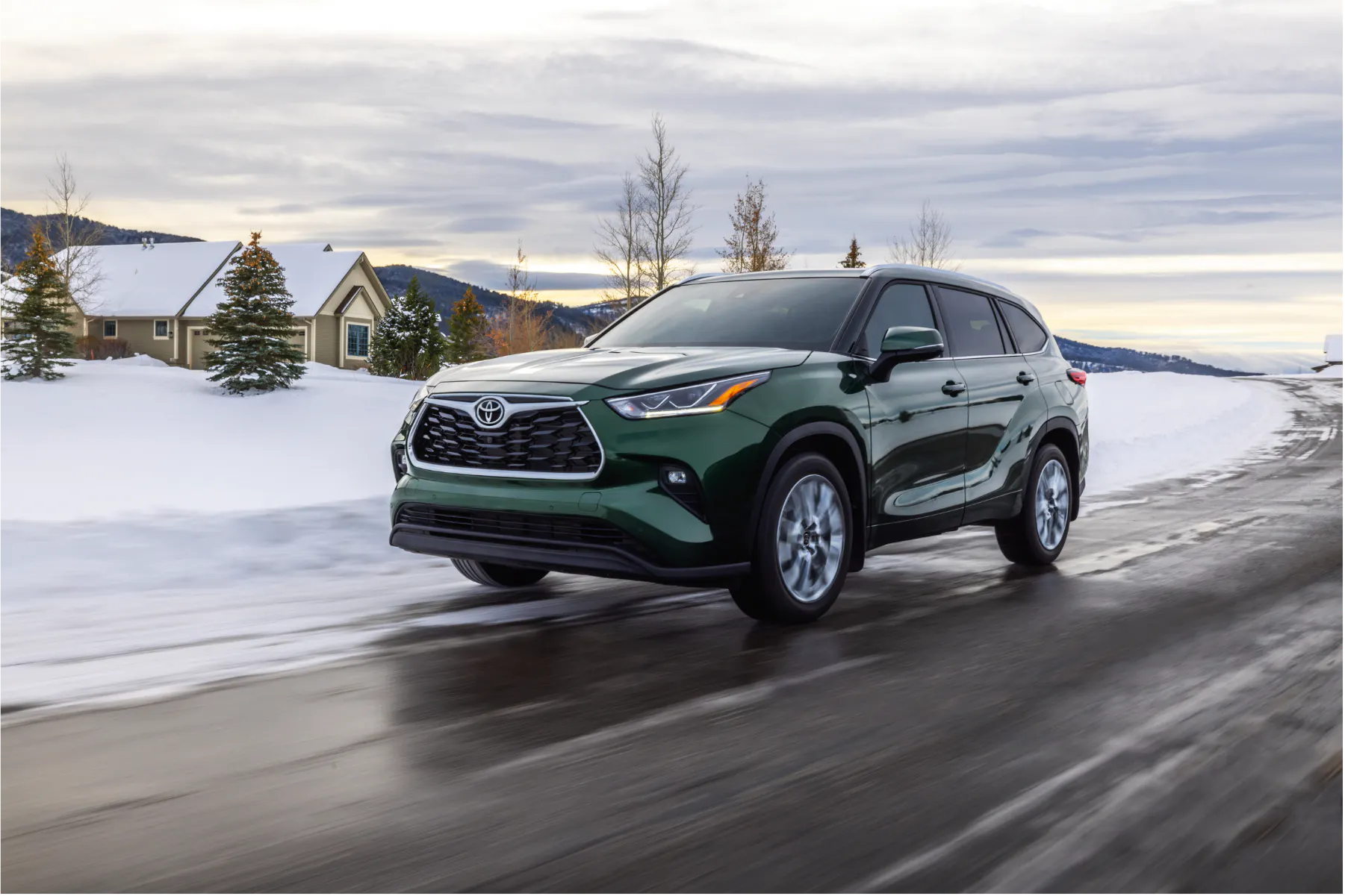 Green Toyota Highlander 3-row SUV driving on a snowy Alaska road with neighborhood houses in the background