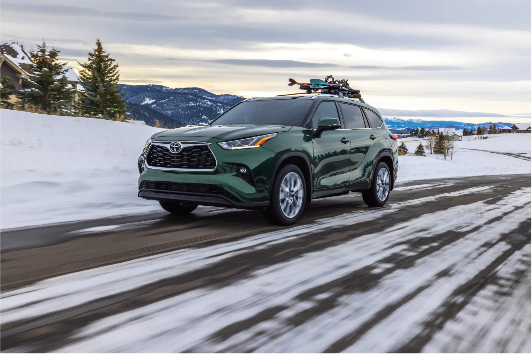 Green Toyota Highlander with skis loaded on the roof rack driving to the mountains