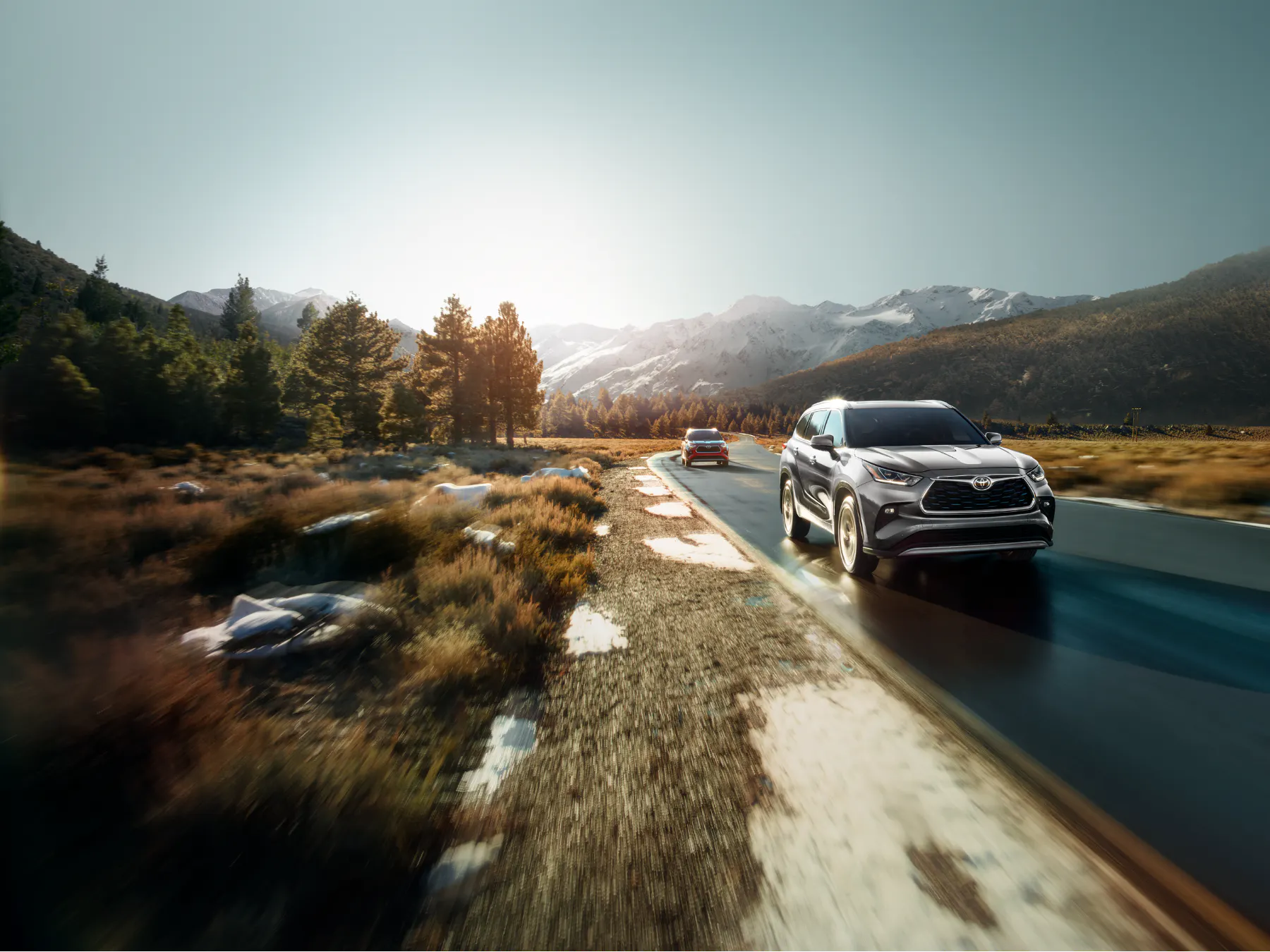 Silver Toyota Highlander driving down a mountain road at sunset
