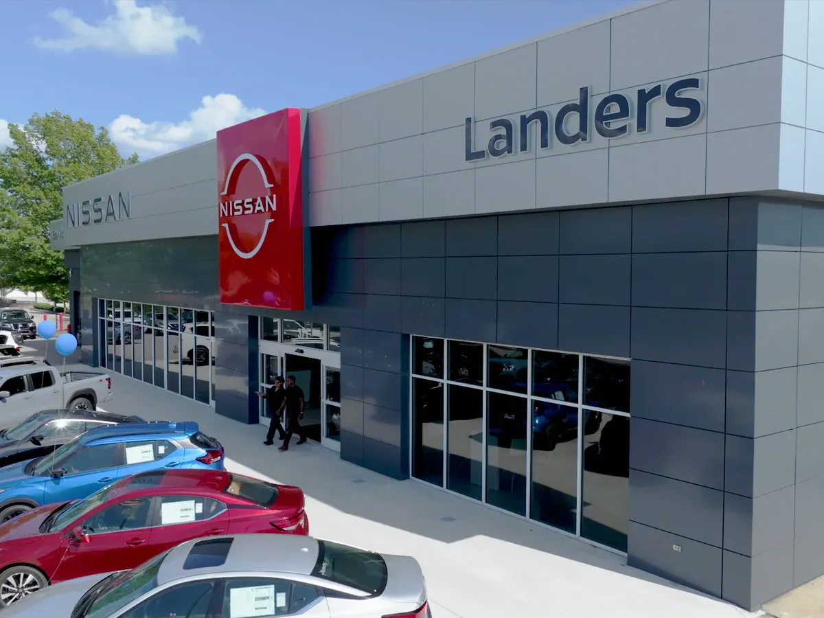 Modern Nissan dealership exterior with Landers branding, large showroom windows, and new vehicles displayed outside on a sunny day.