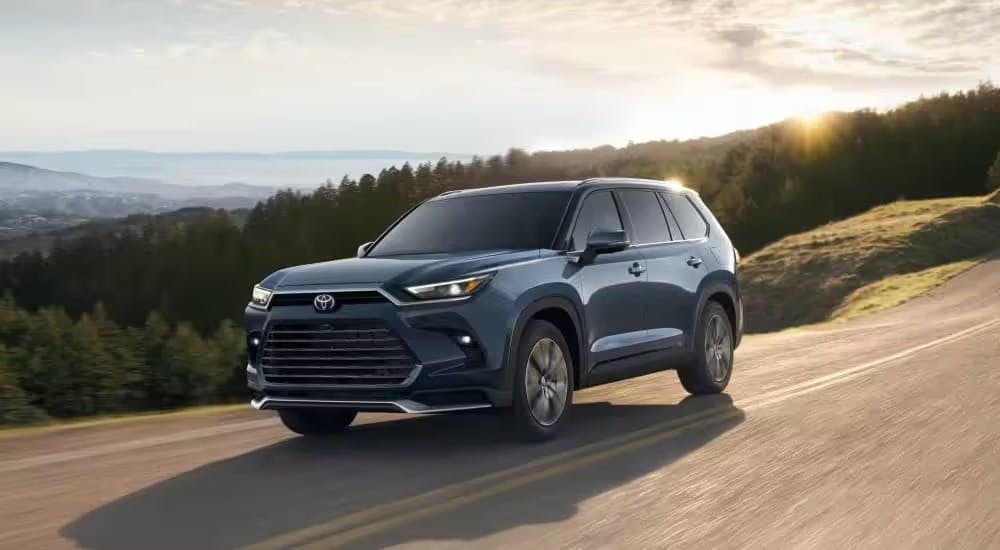 A blue 2024 Toyota Grand Highlander is shown driving after visiting a Toyota dealer near Vinings.