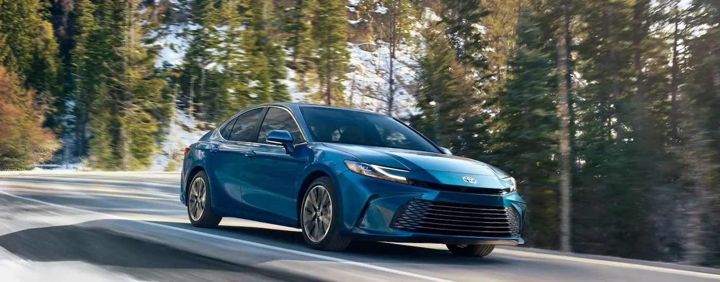 Blue 2026 Toyota Camry driving down a road.