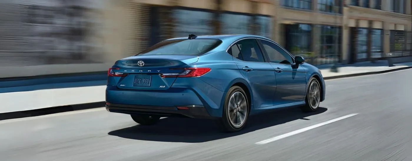 Rear of a blue 2026 Toyota Camry XLE driving down a road.
