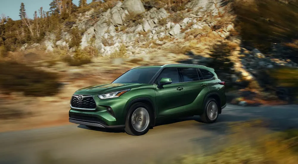 Green 2026 Toyota Highlander driving down a road.