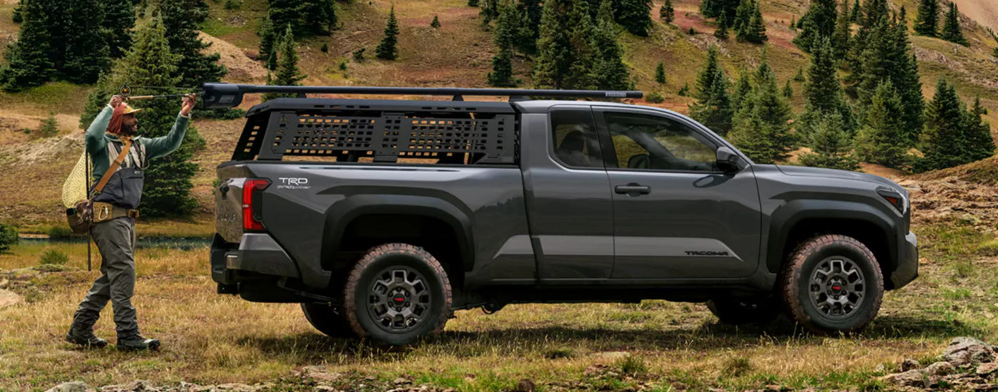 A person getting a fishing rod out of the roof rack on their black 2026 Toyota Tacoma