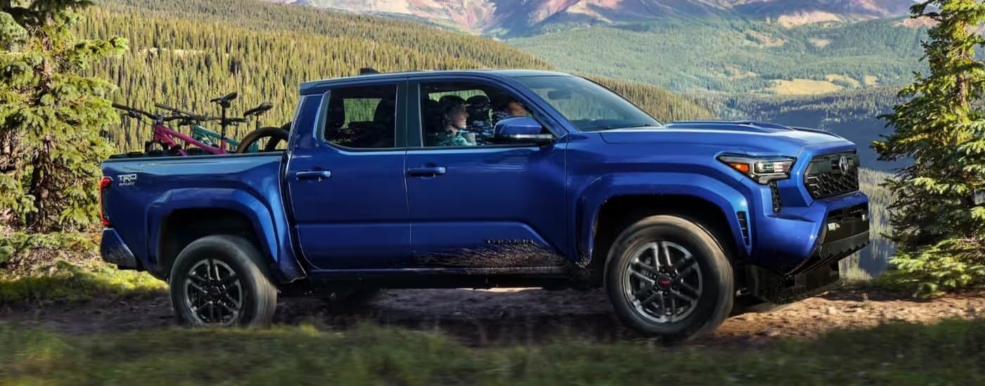 A blue 2025 Toyota Tacoma TRD Sport is shown driving on a dirt trail.