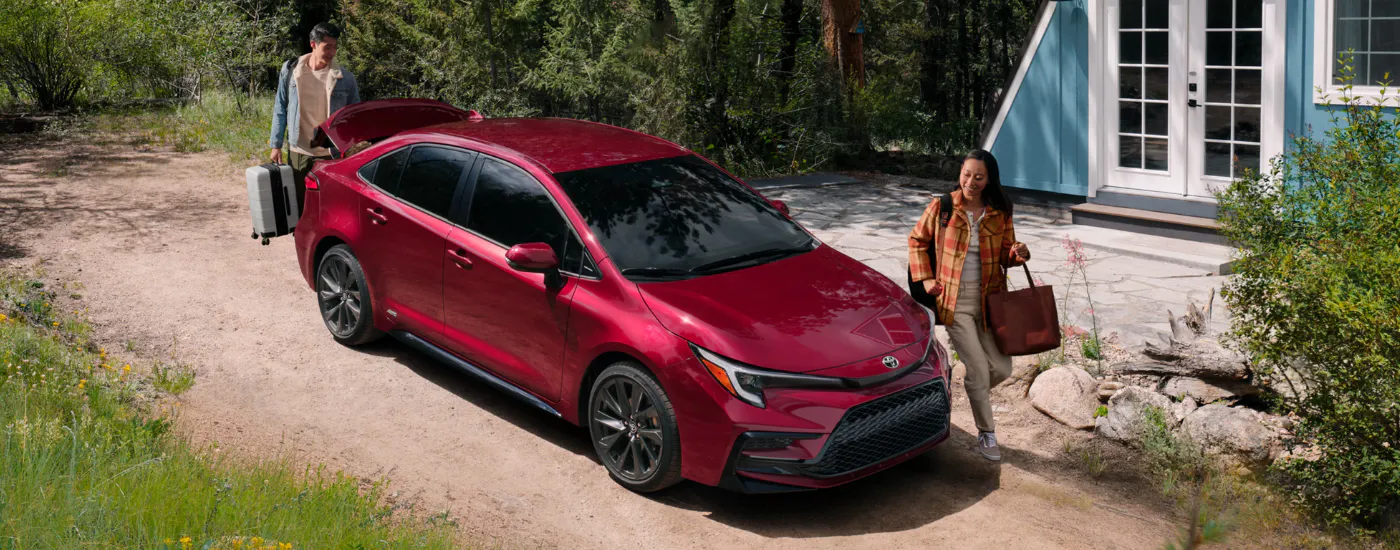 Two people loading luggage into a red 2026 Toyota Corolla
