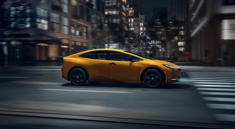 Side of a yellow 2026 Toyota Prius driving down a road.