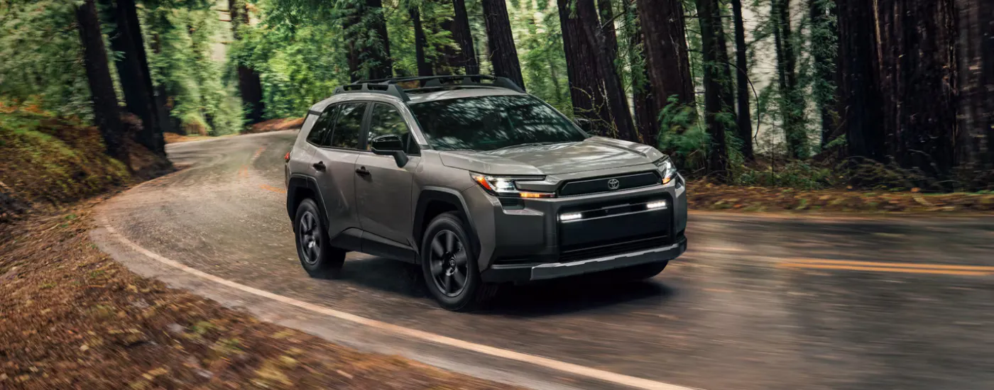 Grey 2026 Toyota RAV4 driving on a winding tree-lined road