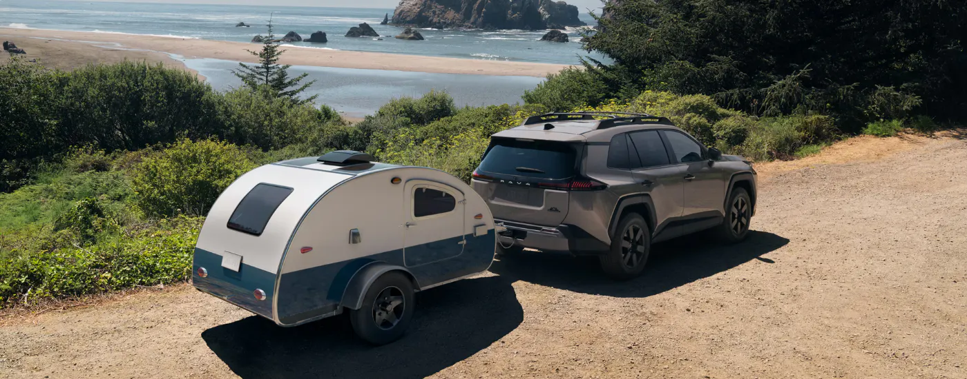 Grey 2026 Toyota RAV4 towing a camper by the water
