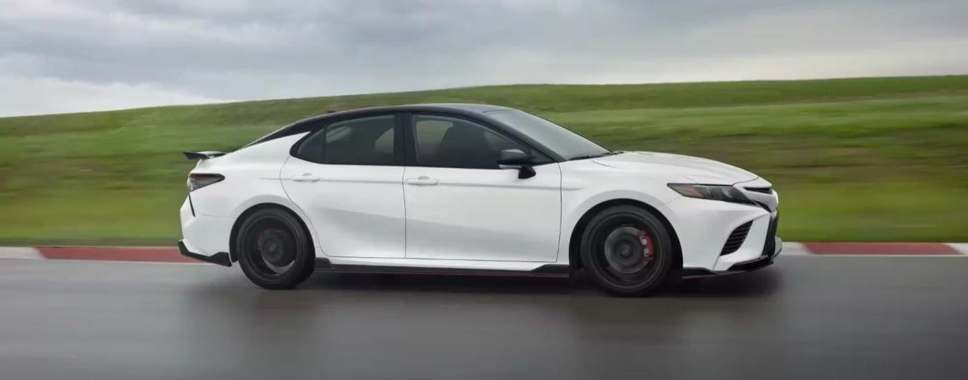 White 2023 Toyota Camry TRD driving near a grassy hill