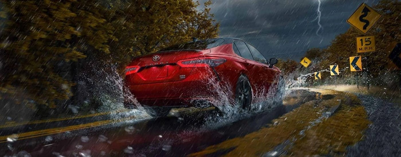 Red 2024 Toyota Camry driving around a rainy bend