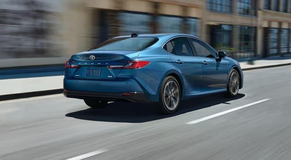 A blue 2025 Toyota Camry XLE is shown driving on a city street.