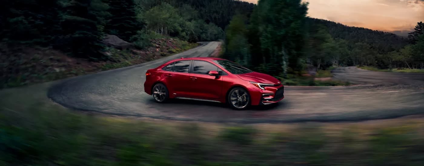 Red 2026 Toyota Corolla Hybrid for sale near Sandy Springs driving around a bend.