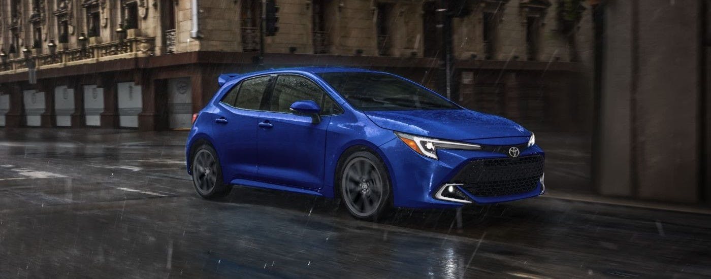Blue 2024 Toyota Corolla driving on a city street in the rain