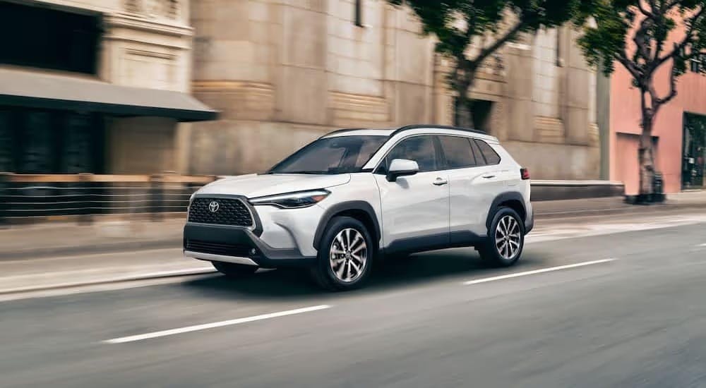 A white 2024 Toyota Corolla Cross is shown driving on a city street.