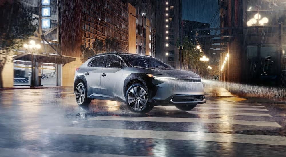 A silver 2024 Toyota bZ4X Limited driving to a Toyota dealer near Kennesaw on a rainy night.