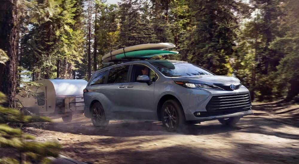 A silver 2024 Toyota Sienna Woodland Edition is shown towing a trailer off-road.