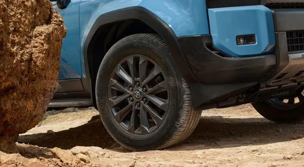 A close-up of a wheel on a blue 2024 Toyota Land Cruiser is shown.