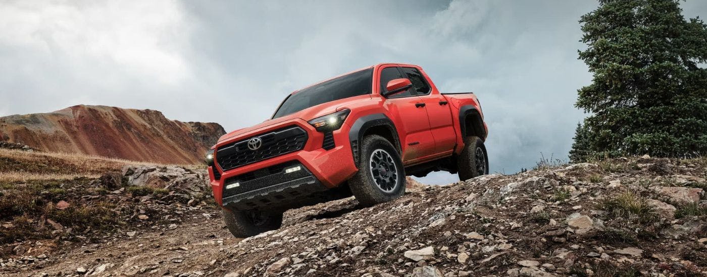 Orange 2025 Toyota Tacoma TRD Off-Road driving off-road down a hill.