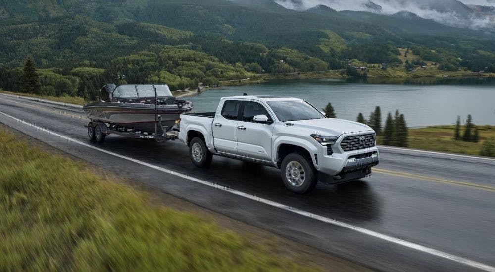 A white 2025 Toyota Tacoma for sale near Roswell is shown towing a boat near a lake.