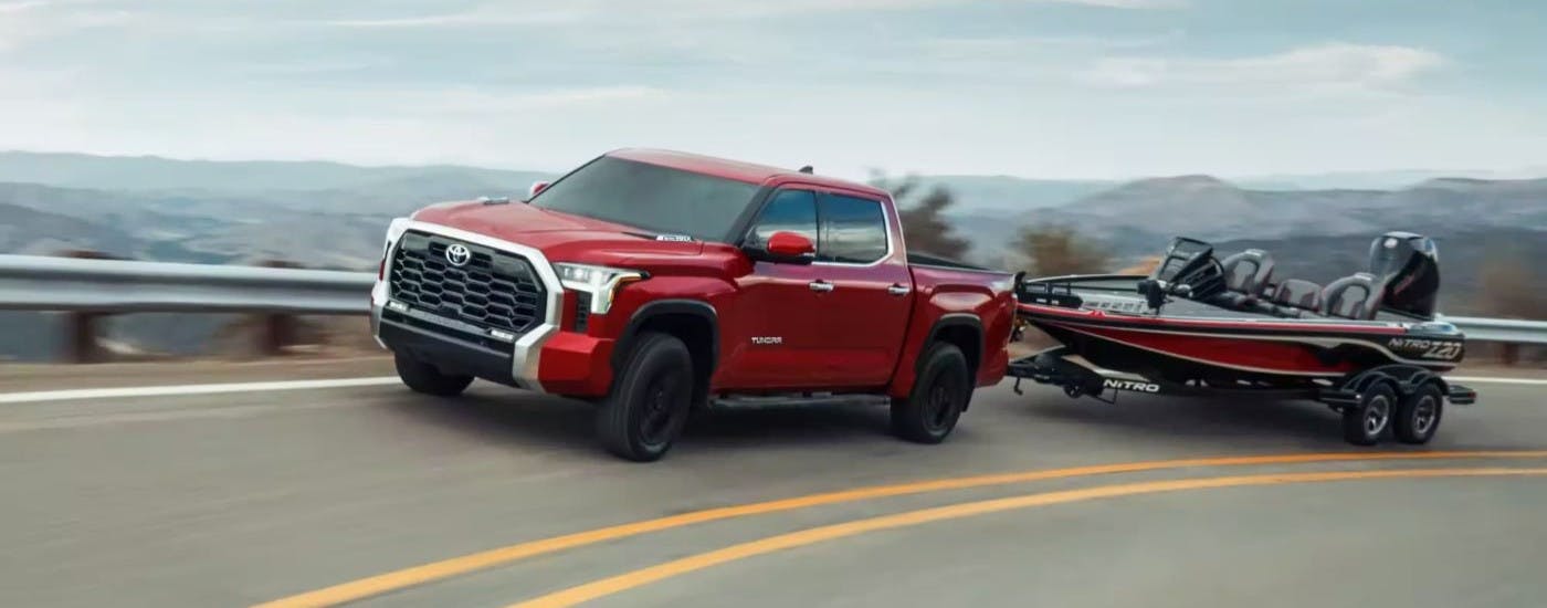 Red 2024 Toyota Tundra towing a boat on a highway