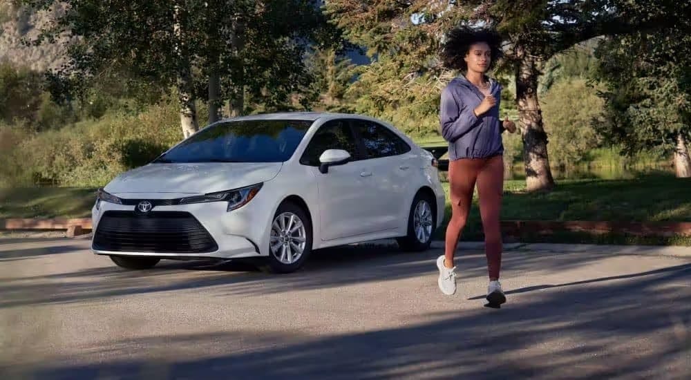 A jogger near a parked white 2023 Toyota Corolla.