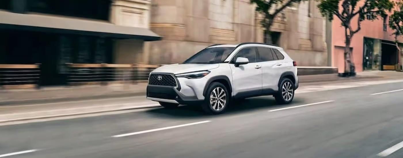 A white 2023 Toyota Corolla Cross Hybrid is shown driving to a used Toyota dealer near Vinings.