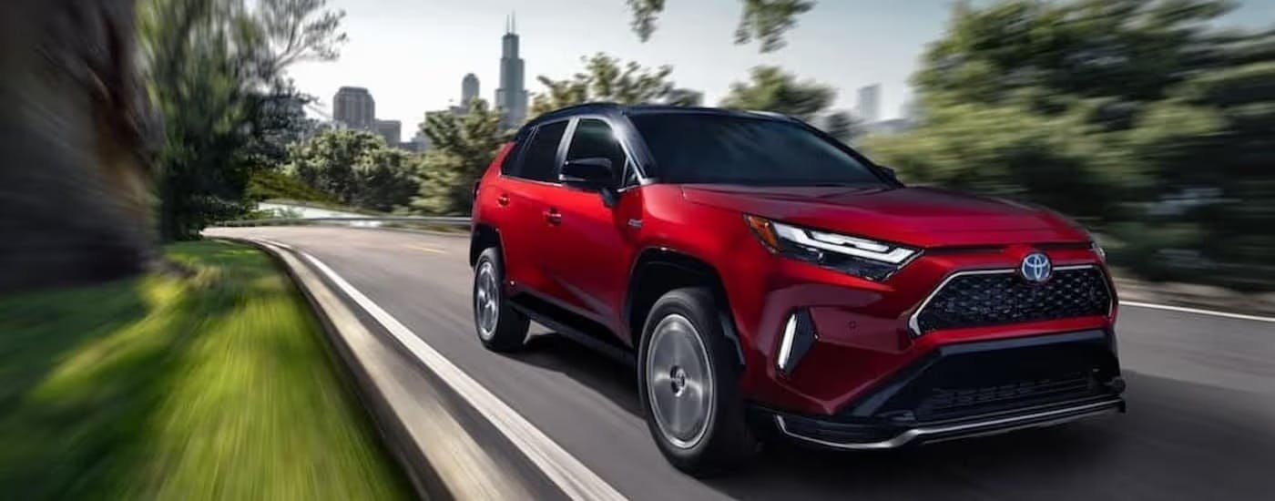 A red 2023 Toyota RAV4 Prime is shown driving near a city.