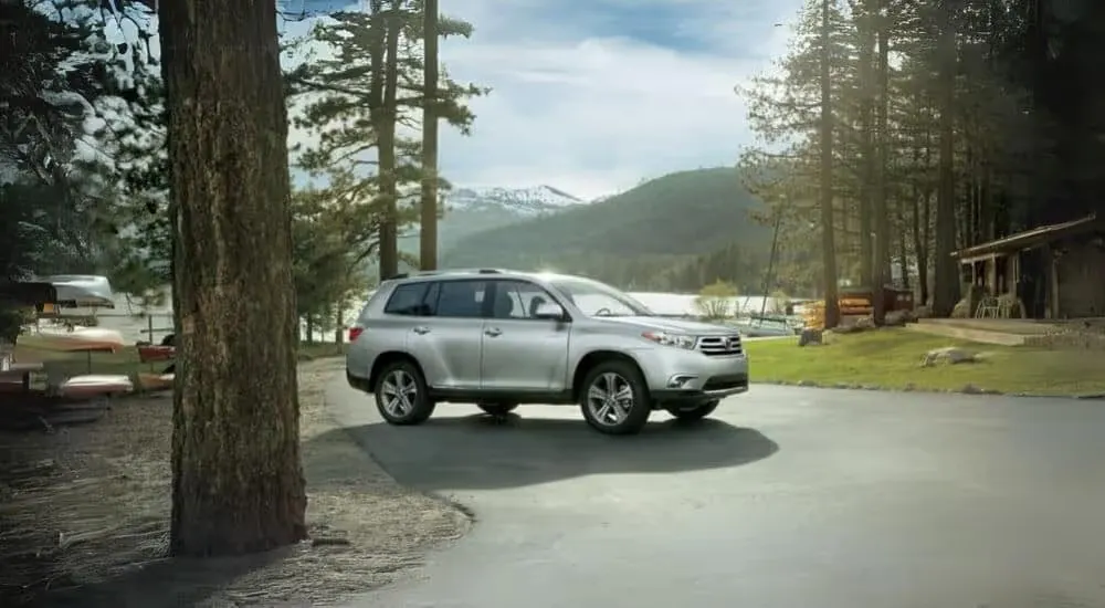 A silver 2013 used Toyota Highlander for sale is shown parked near a lake.