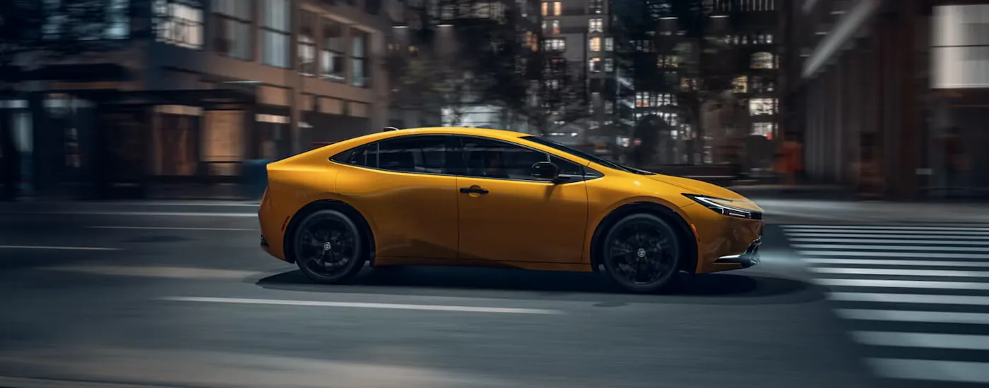 Side of a yellow 2026 Toyota Prius driving down a road.