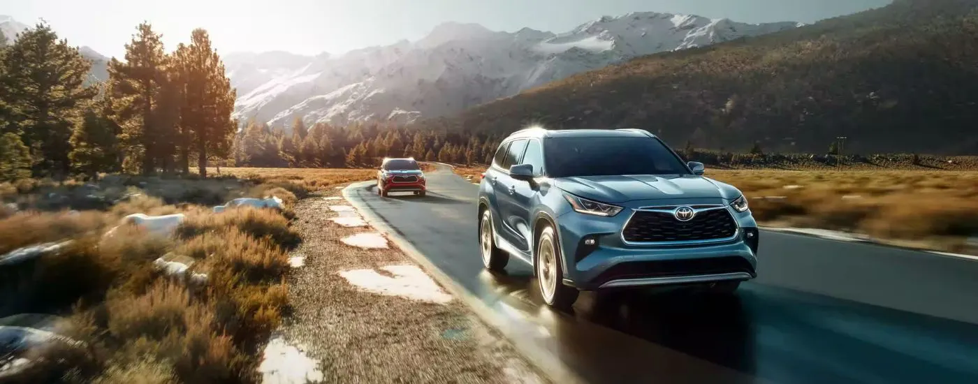 Blue 2023 Toyota Highlander driving down an open road with a red 2023 Toyota Highlander following