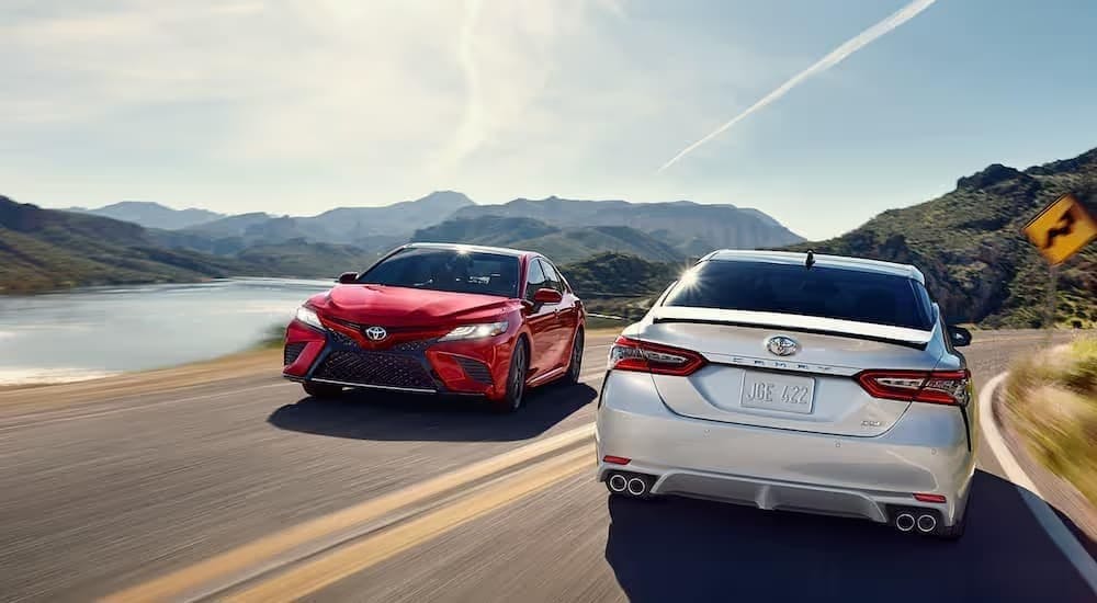 A red and a white Toyota Camry passing each other on a highway.
