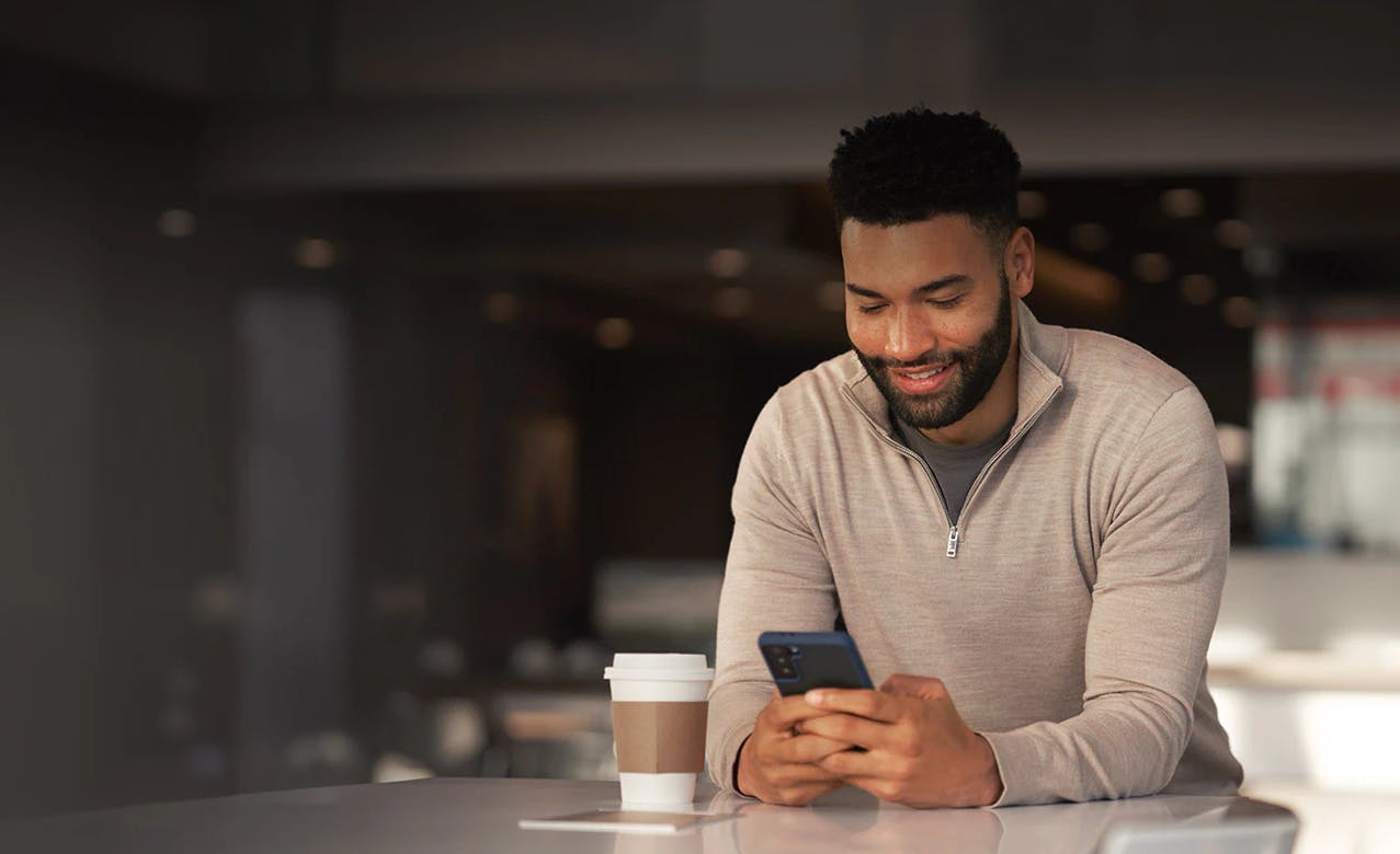online-financing-application Person smiling while looking at phone at table with coffee