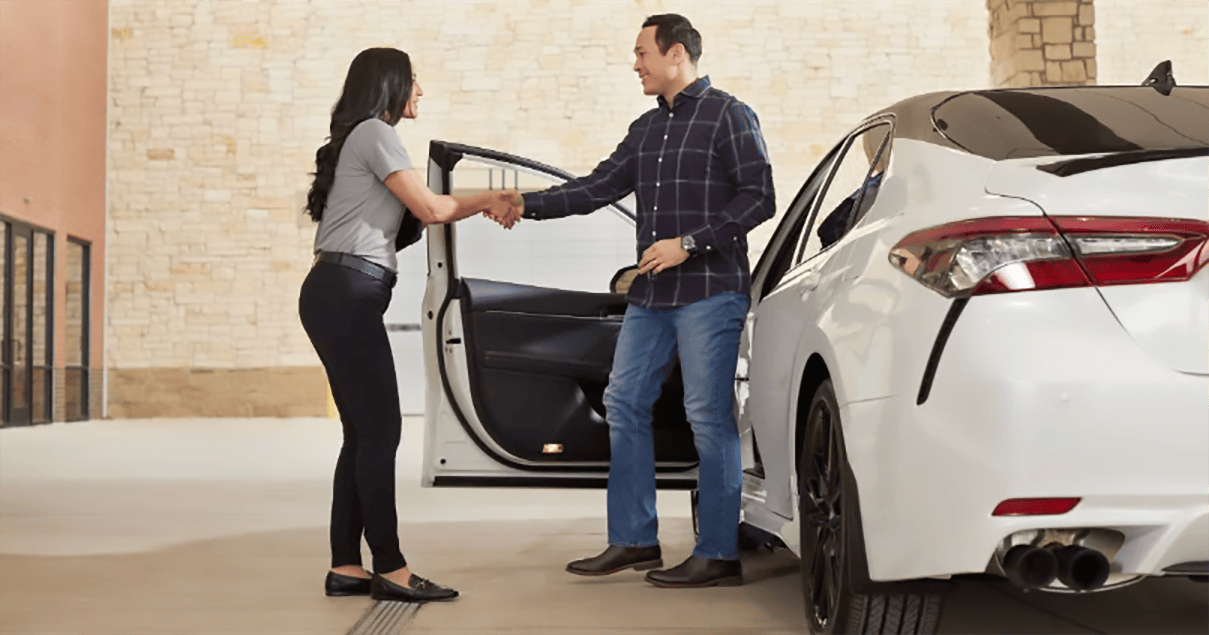 Women sales advisor shakes hand of man getting out of new car