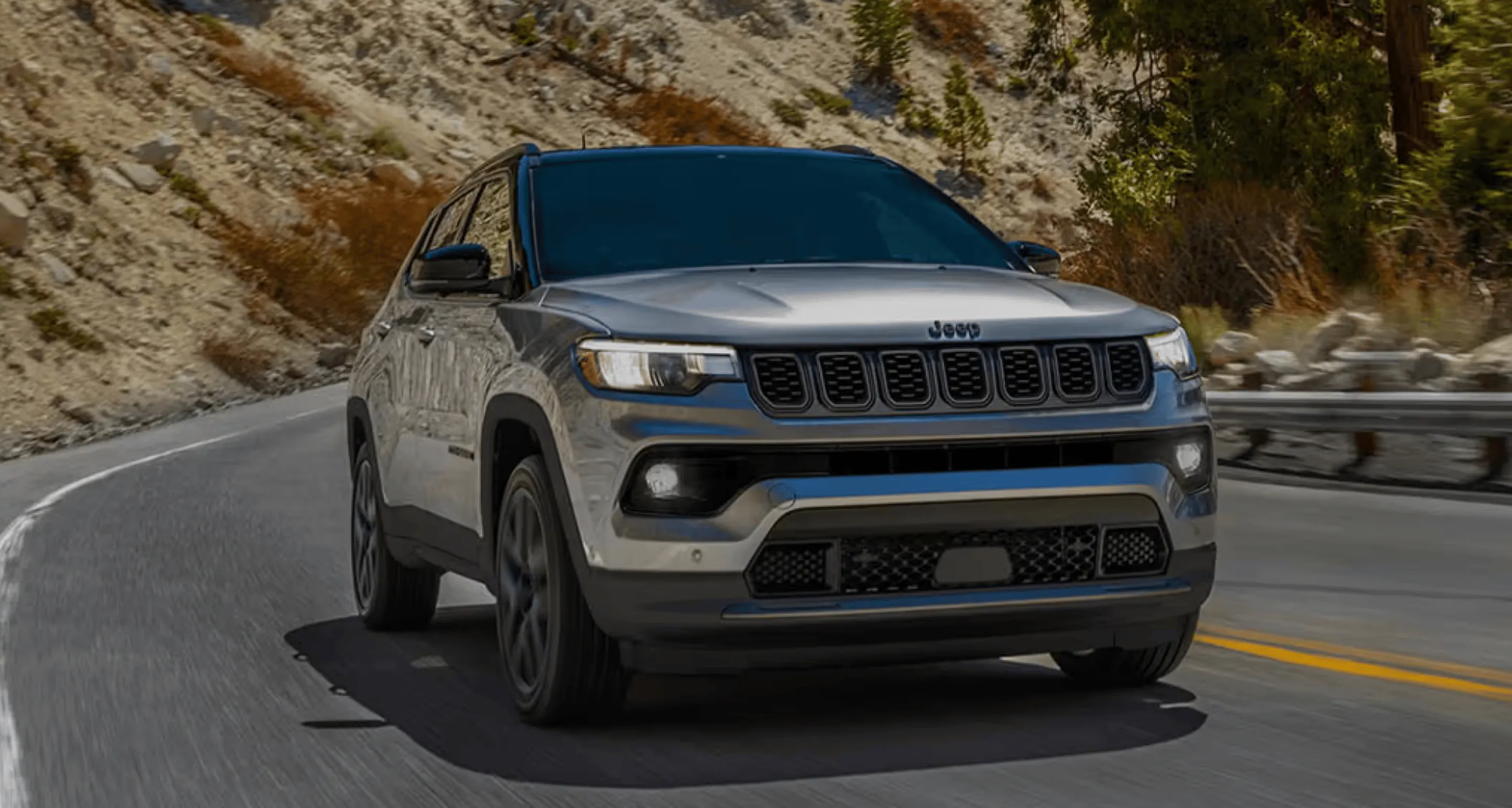 Gray Jeep SUV driving around a curved mountain road bordered by rocks and trees.