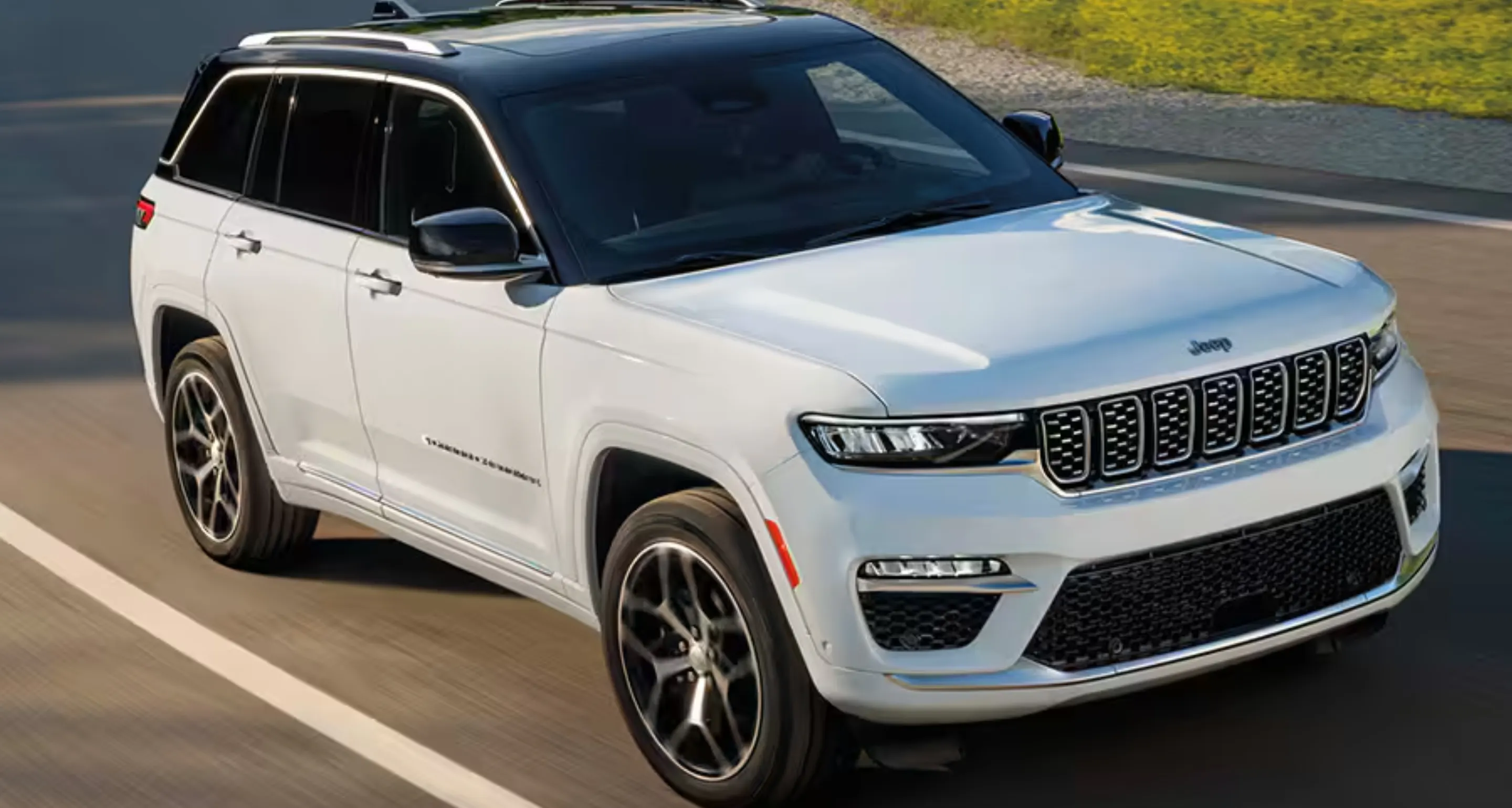 White Jeep SUV with a black roof driving on a paved road, viewed from the front side.