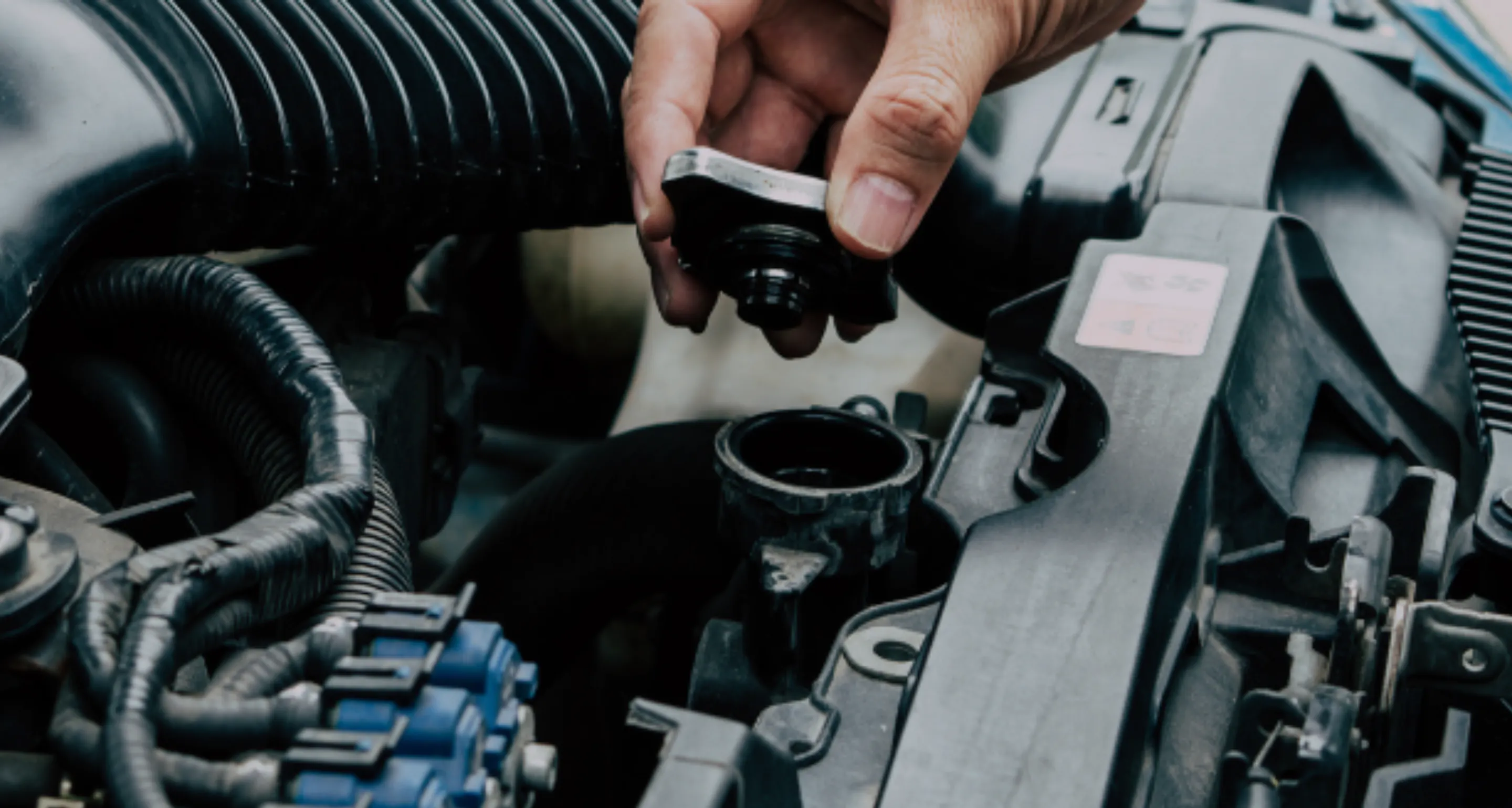Close-up of a hand removing a cap from an open reservoir inside a vehicle engine compartment.