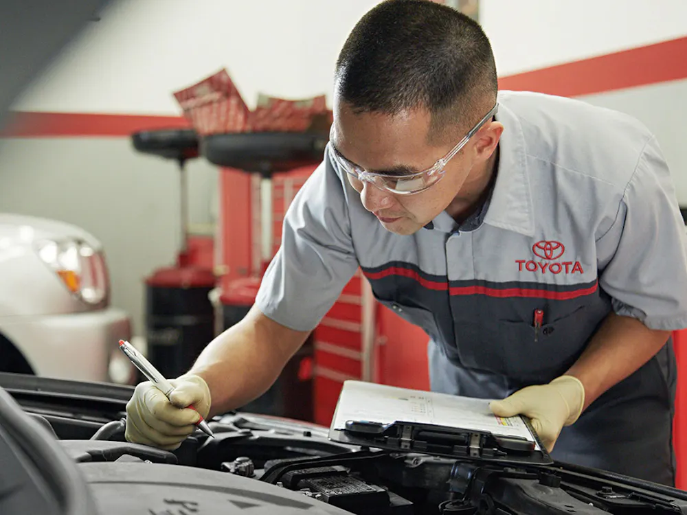 Toyota service technician writing a service report beside a vehicle